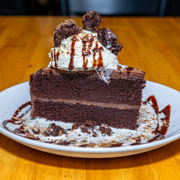 A slice of Lost Lion's rich chocolate cake with whipped cream, chocolate drizzle, and brownie pieces.
