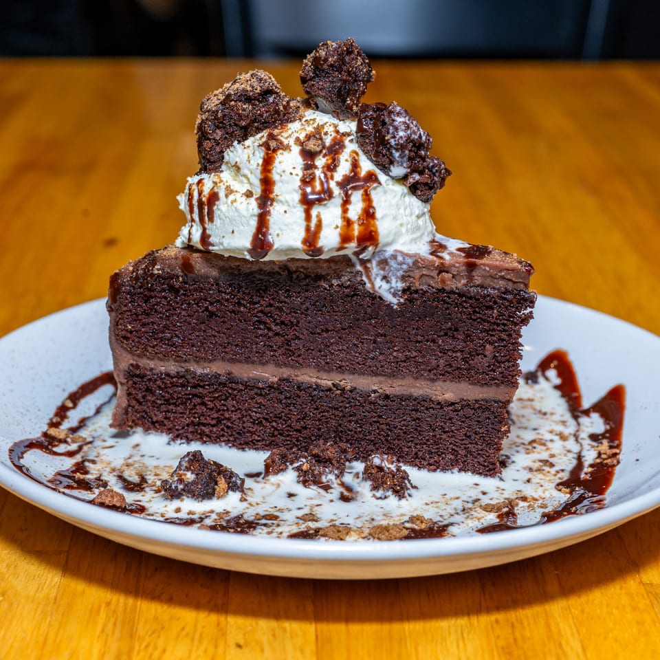 A slice of Lost Lion's rich chocolate cake with whipped cream, chocolate drizzle, and brownie pieces.