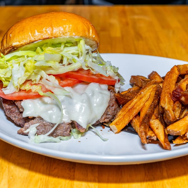 Lost Lion's cheesesteak sandwich with melted white cheese, lettuce, tomatoes, and a side of fries.