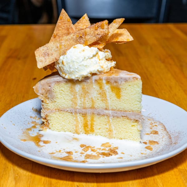 Lost Lion's Tres Leches cake slice with whipped cream, caramel drizzle, and cinnamon sugar chips.