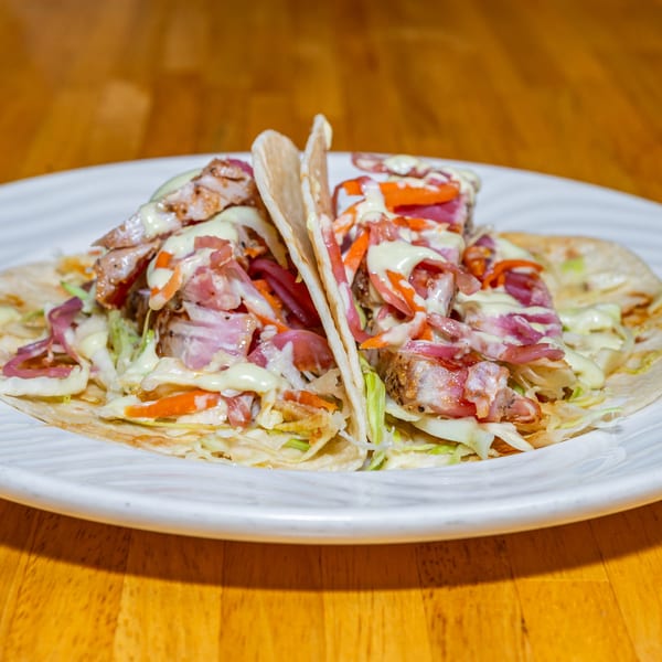 Two Lost Lion tacos with grilled meat, shredded cabbage, pickled onions, and creamy sauce on a white plate.