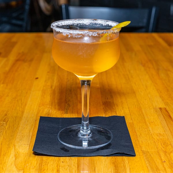 Lost Lion's amber cocktail with a salted rim and lemon twist on a wooden table.