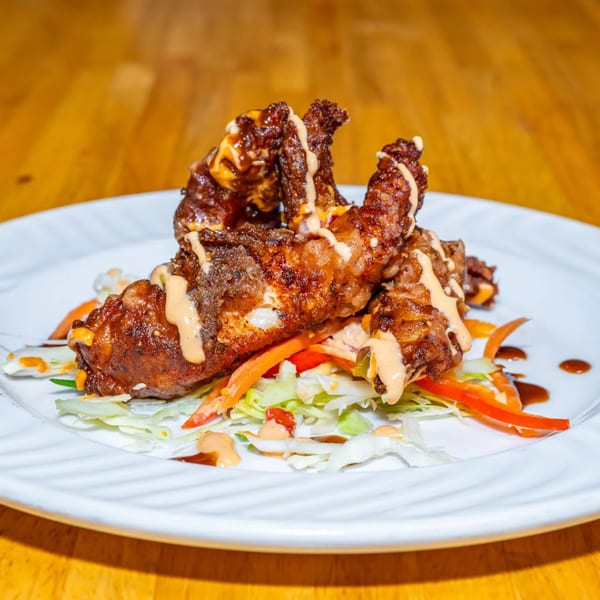 Crispy fried chicken tenders drizzled with sauce, served on a bed of shredded lettuce and bell peppers.