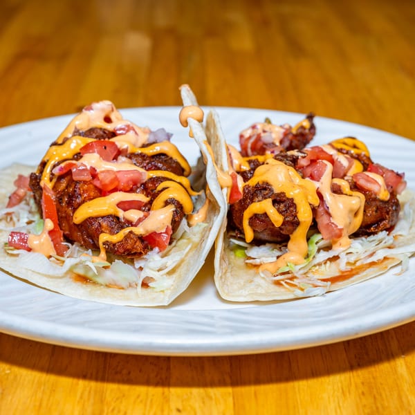 Two Lost Lion tacos with fried chicken, shredded lettuce, diced tomatoes, and creamy sauces.